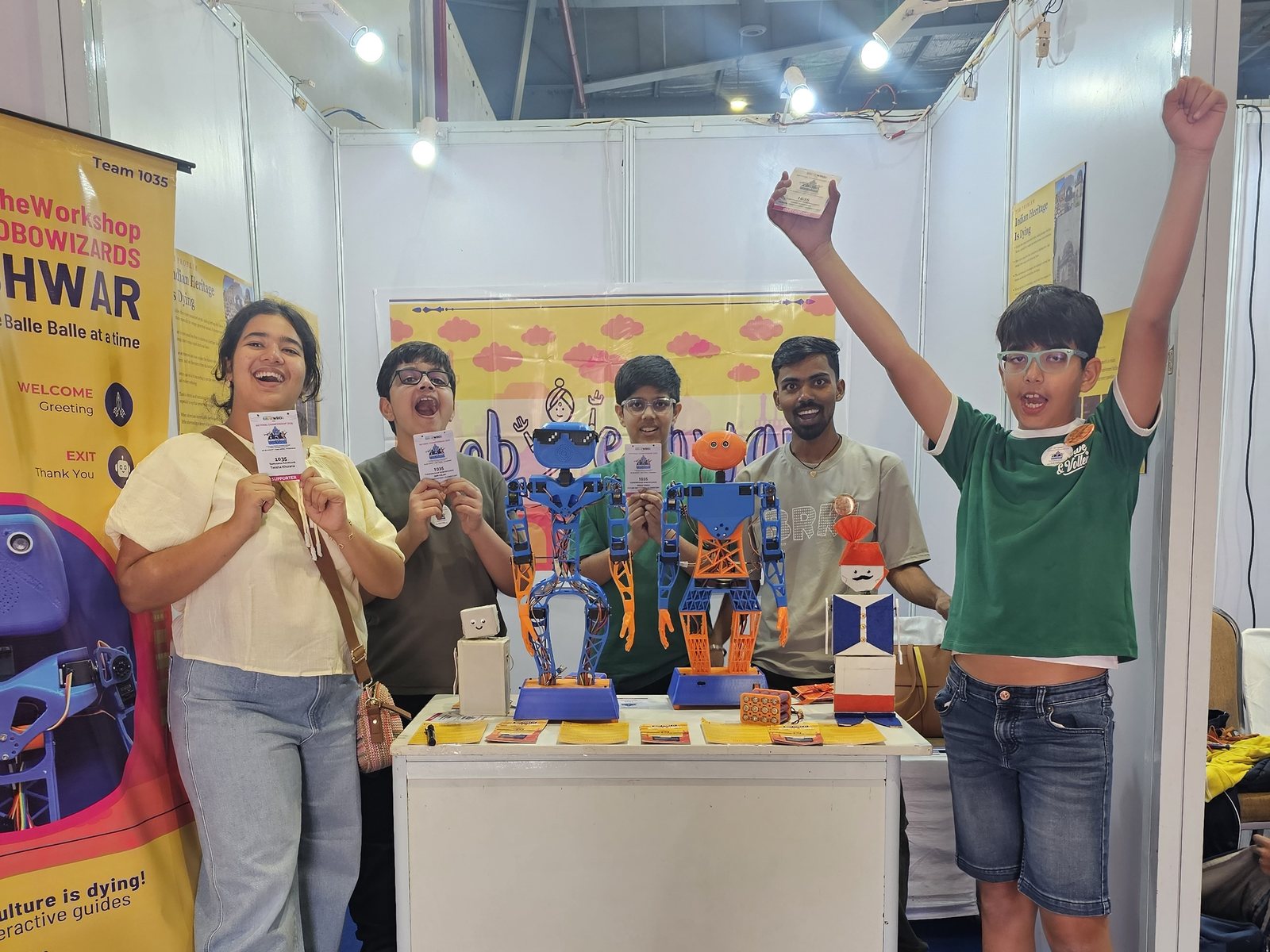 TheWorkshop students and their mentor celebrating beside the robots they built for a competition.