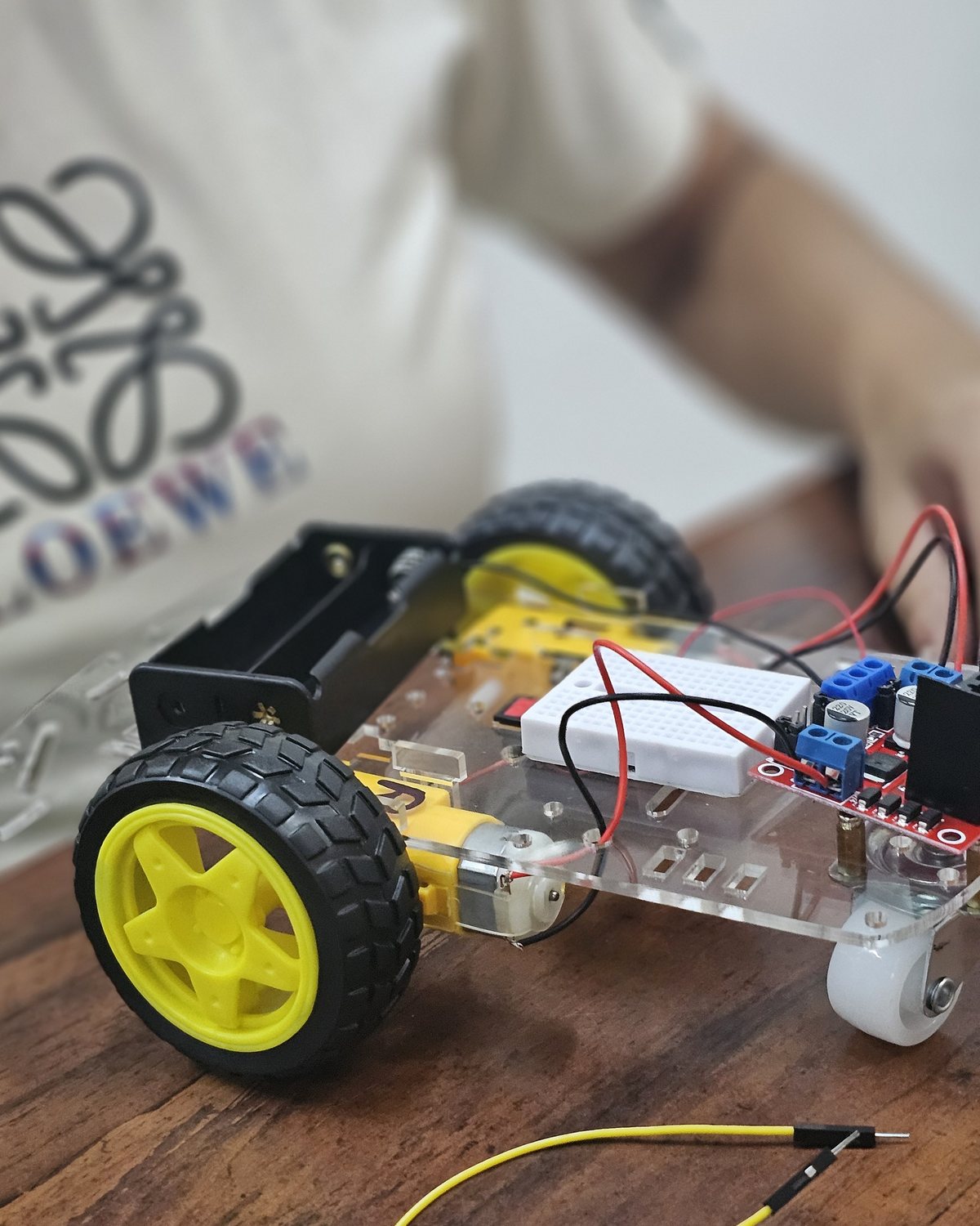 A student's hands connecting a motor and wiring during an After-School Robotics Club session, notebook and circuit board on the desk in front of them.