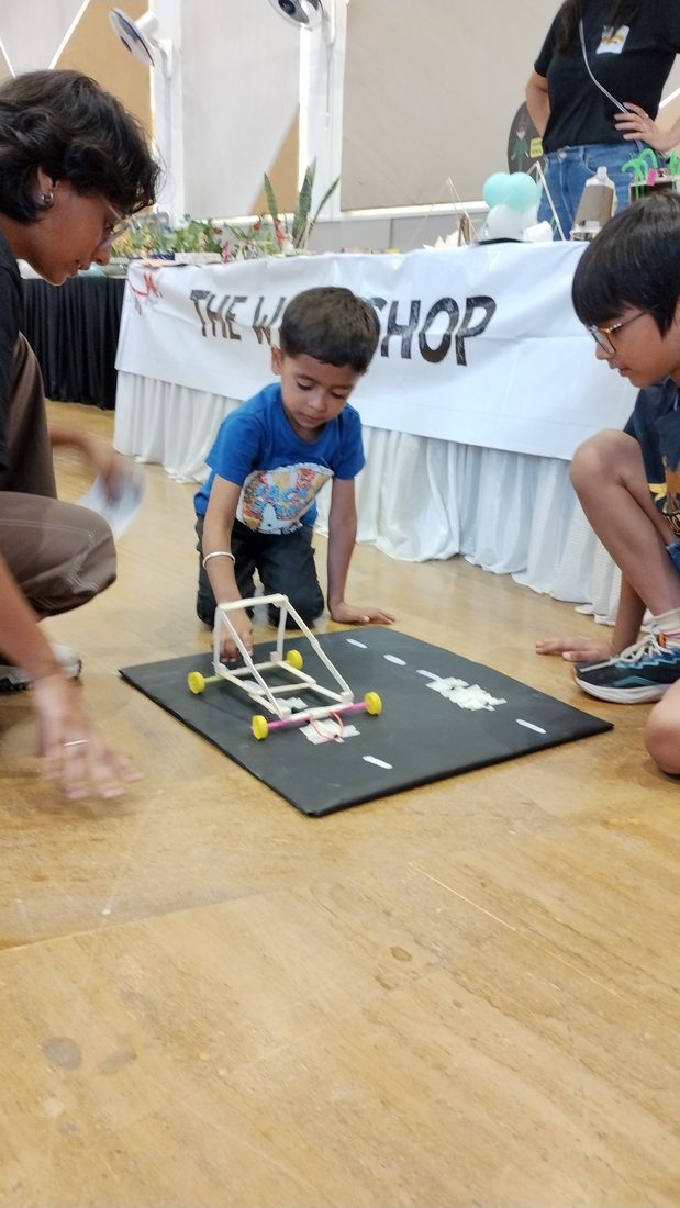 A water-rocket car demo on a cardboard track, with TheWorkshop banner in the background.