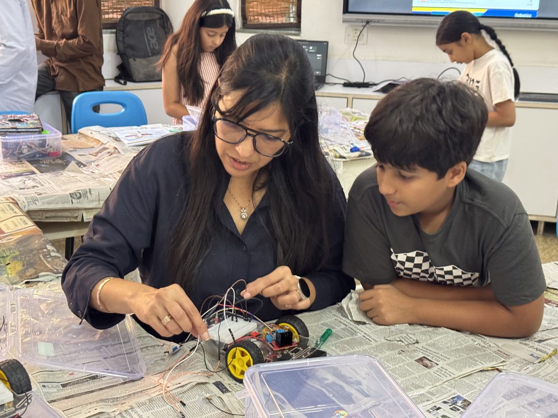 A mentor helping a student wire a small robot car with jumper wires at a table.