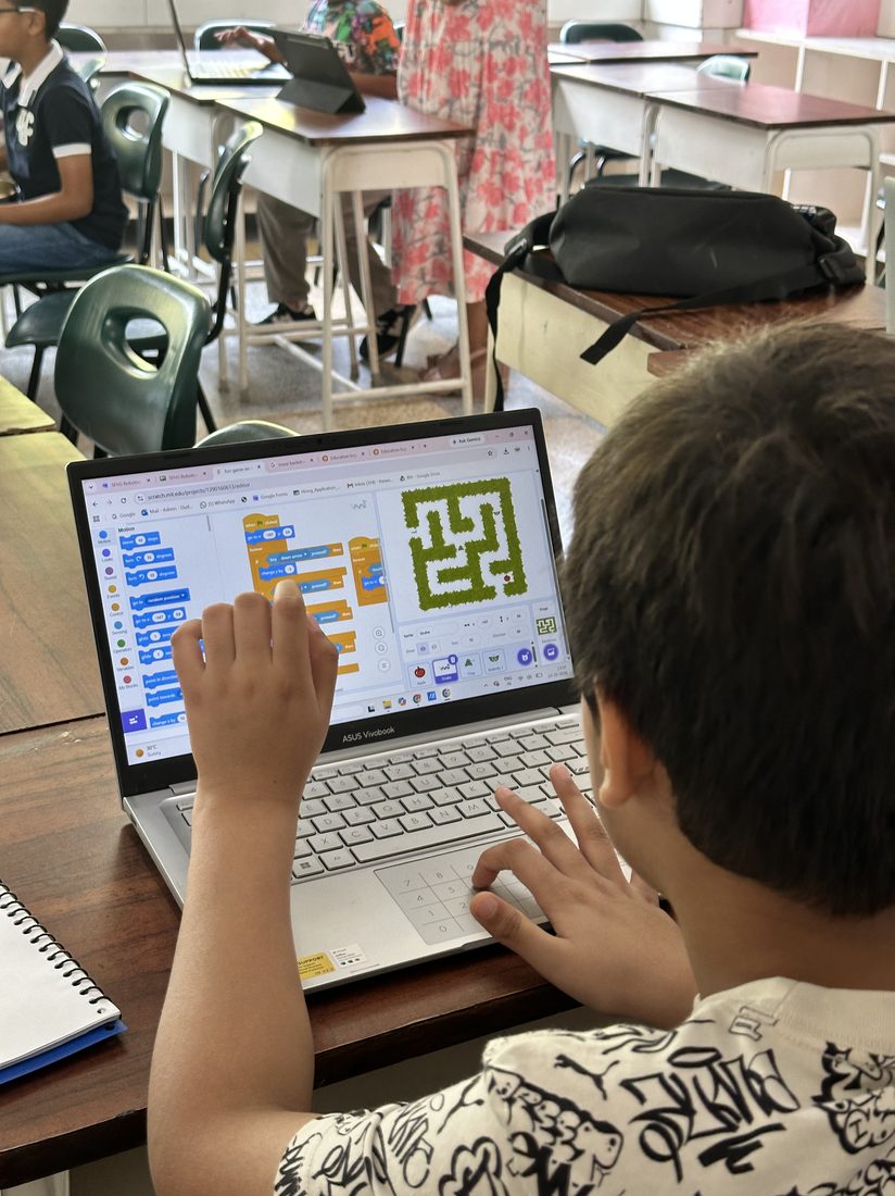 A student coding a maze game in Scratch on a laptop.