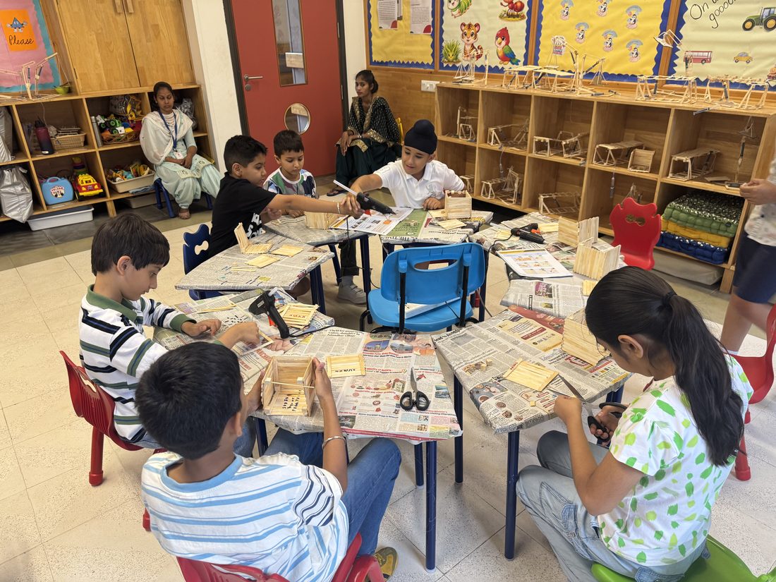 Children building craft structures with hot glue guns at classroom tables.