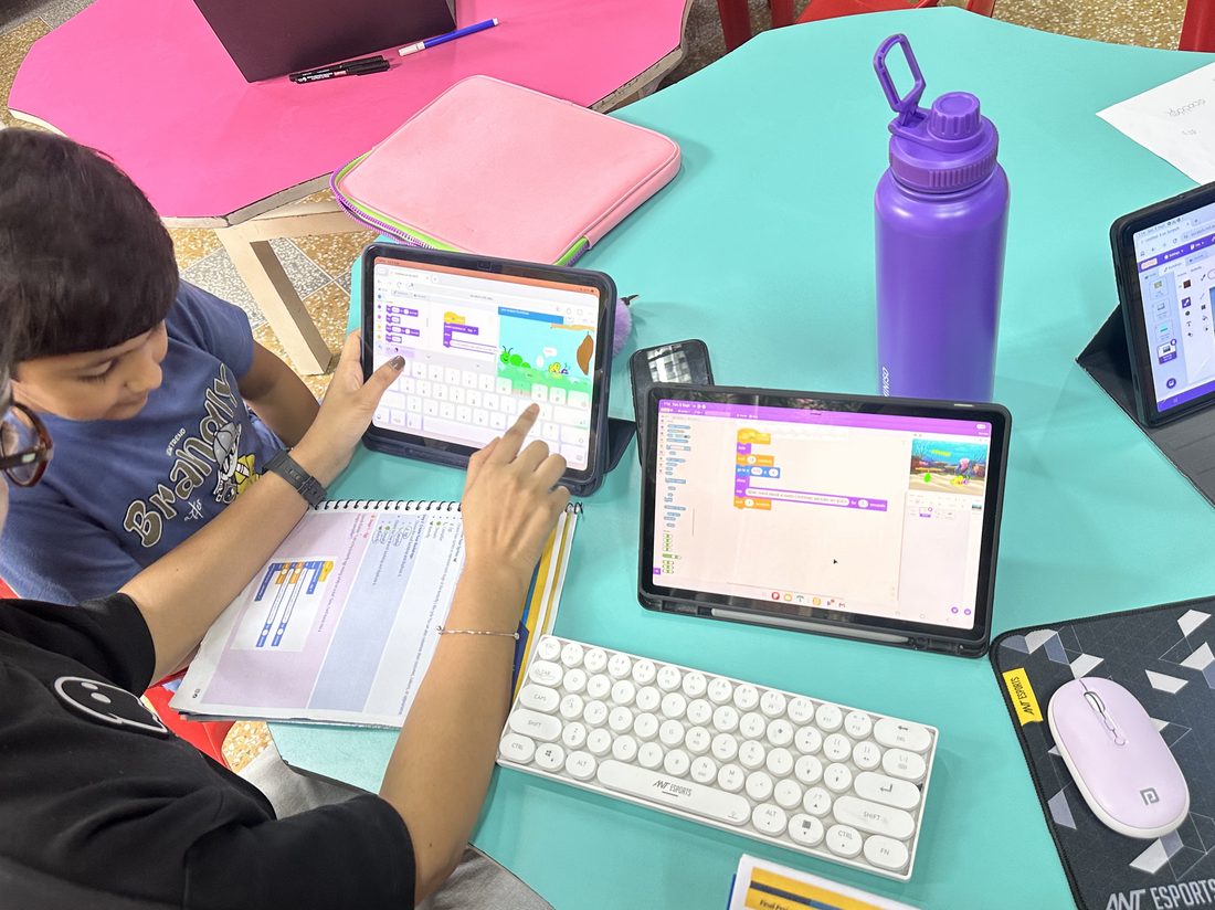 A student coding on two tablets at a colorful table during a Scratch session.