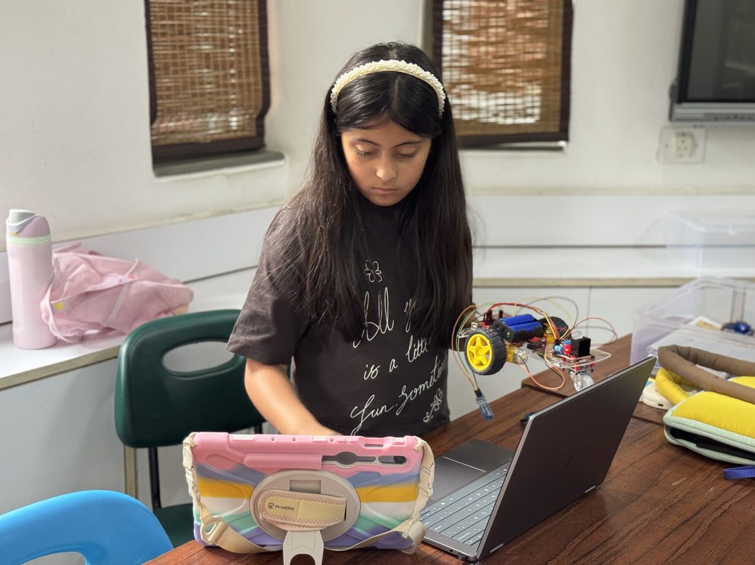 A student standing at a table working on a laptop and a small wired robot.