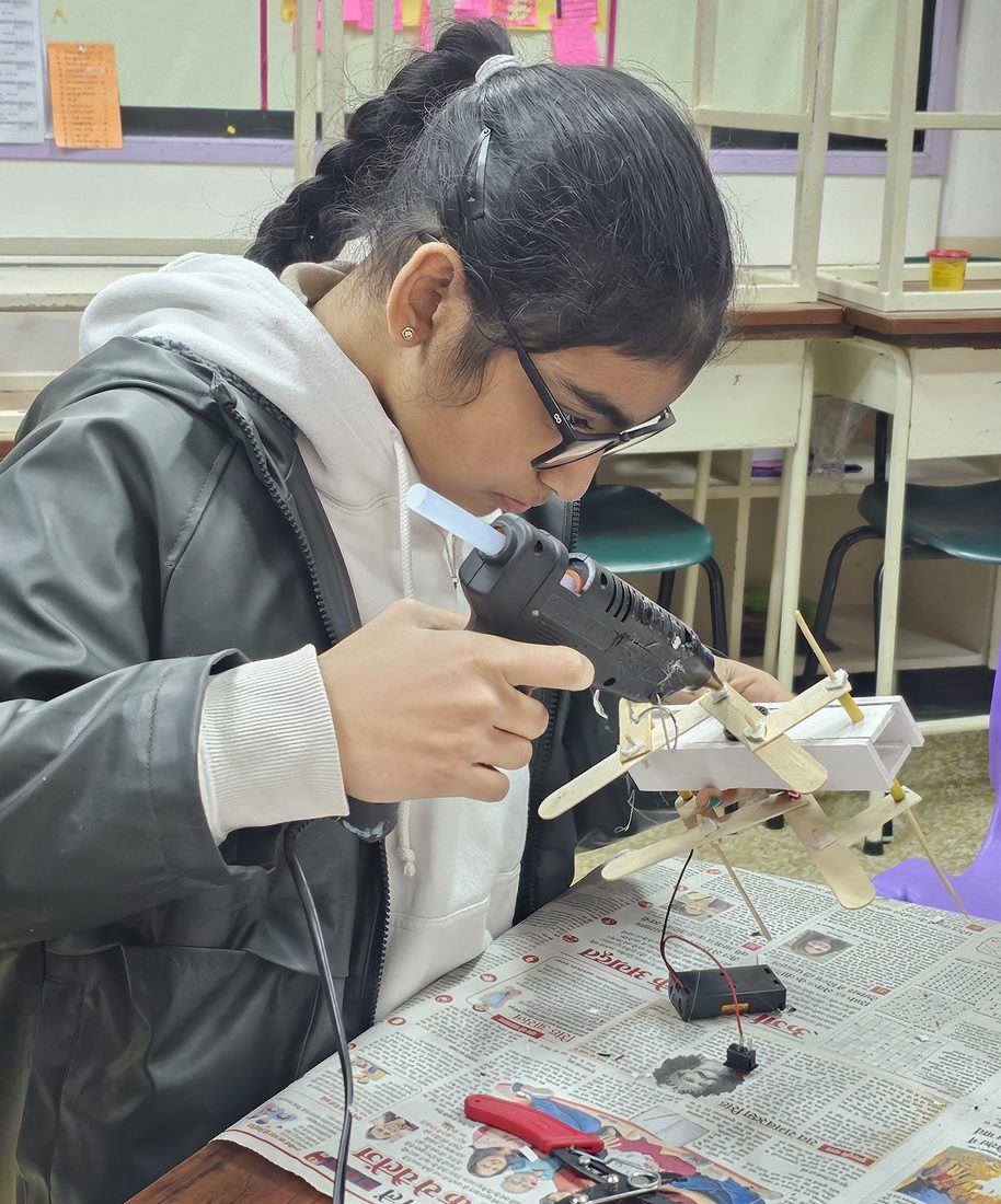 A student using a hot glue gun to build a popsicle-stick structure.