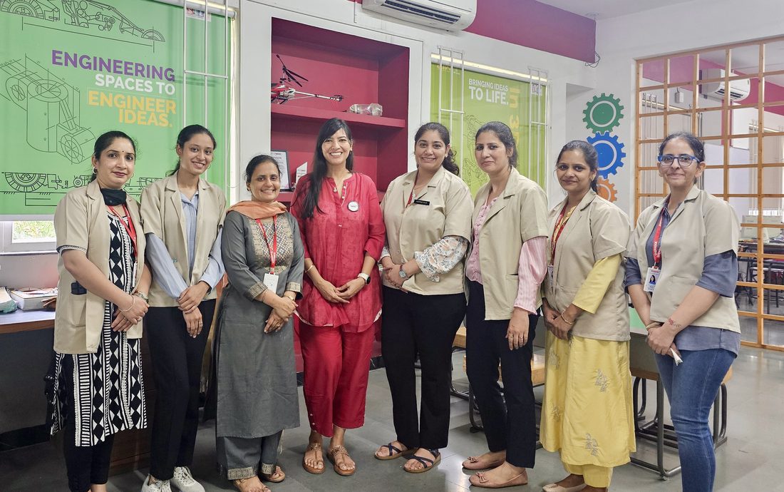 Teachers posing together in front of an 'Engineering Spaces to Engineer Ideas' branded wall after a training session.