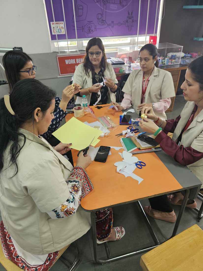 Teachers building a paper craft activity together at a worktable.