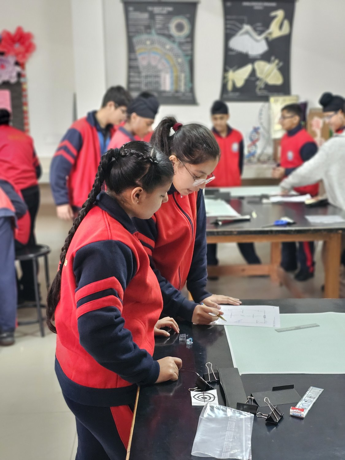 Students measuring and marking out a technical drawing on graph paper at their workbench.