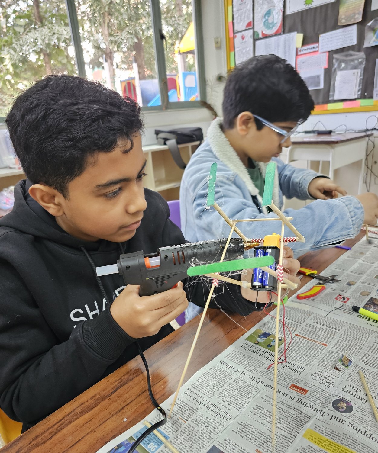 A student using a hot glue gun to assemble a wood-and-wire structure on his own bottle-rocket build.