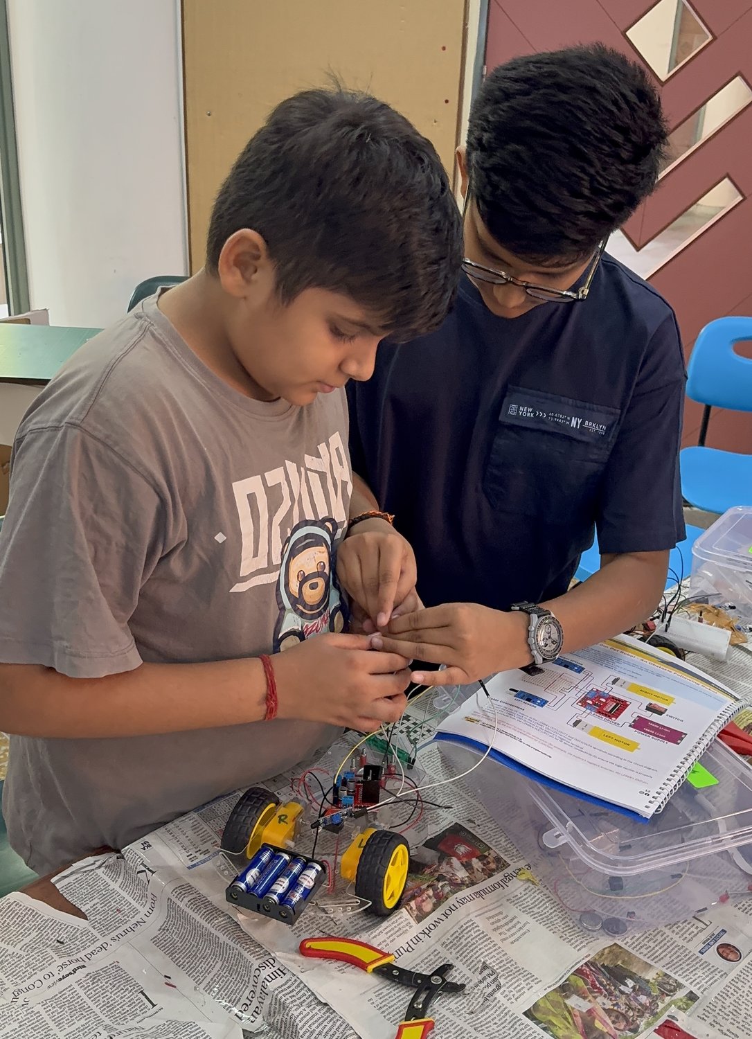 Two students working together to wire up a robot car chassis, tracing the circuit step by step.